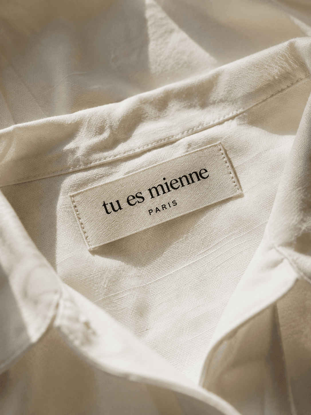 A close-up of the woven "tu es mienne, Paris" label sewn into the collar of a white cotton shirt.